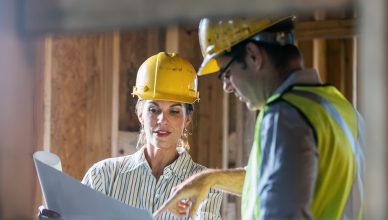 Um homem e uma mulher, em uma construção olhando para uma planta de construção