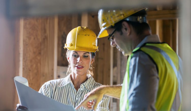 Um homem e uma mulher, em uma construção olhando para uma planta de construção