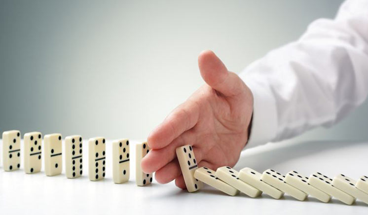Mão humana interrompendo o fluxo de queda de uma fila de dominós